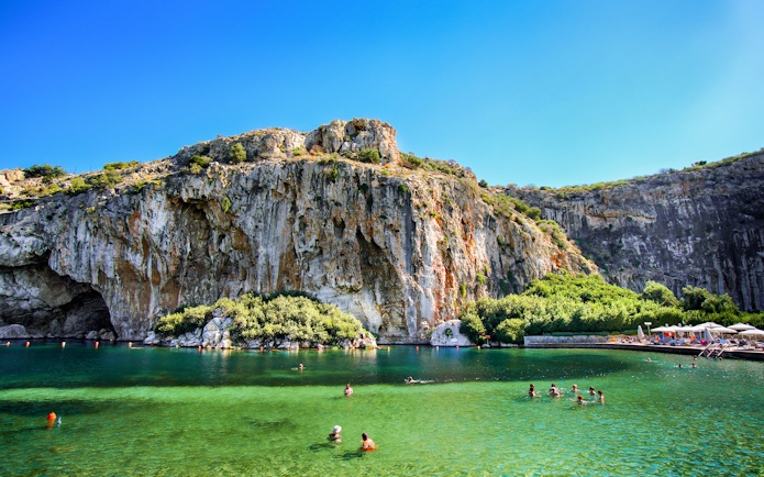 Swimmers enjoying Vouliagmeni Lake near Athens with rocky cliffs and greenery.