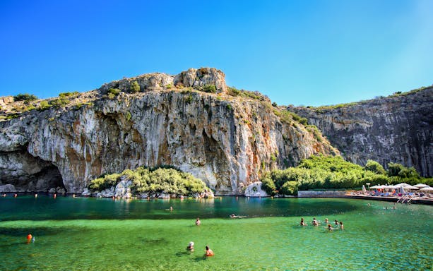 Swimmers enjoying Vouliagmeni Lake near Athens with rocky cliffs and greenery.