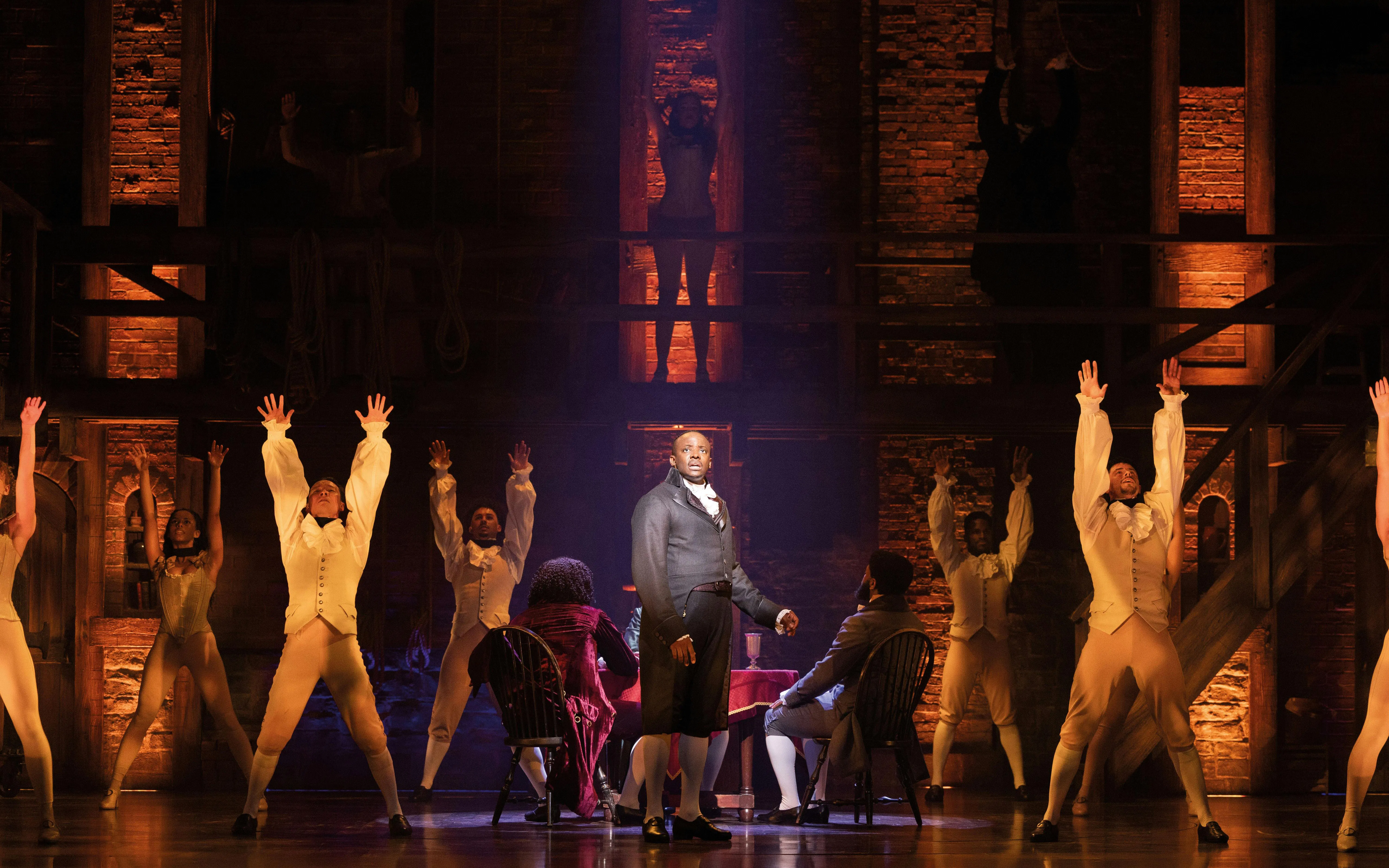 Hamilton cast performing on West End stage with actors in period costumes.