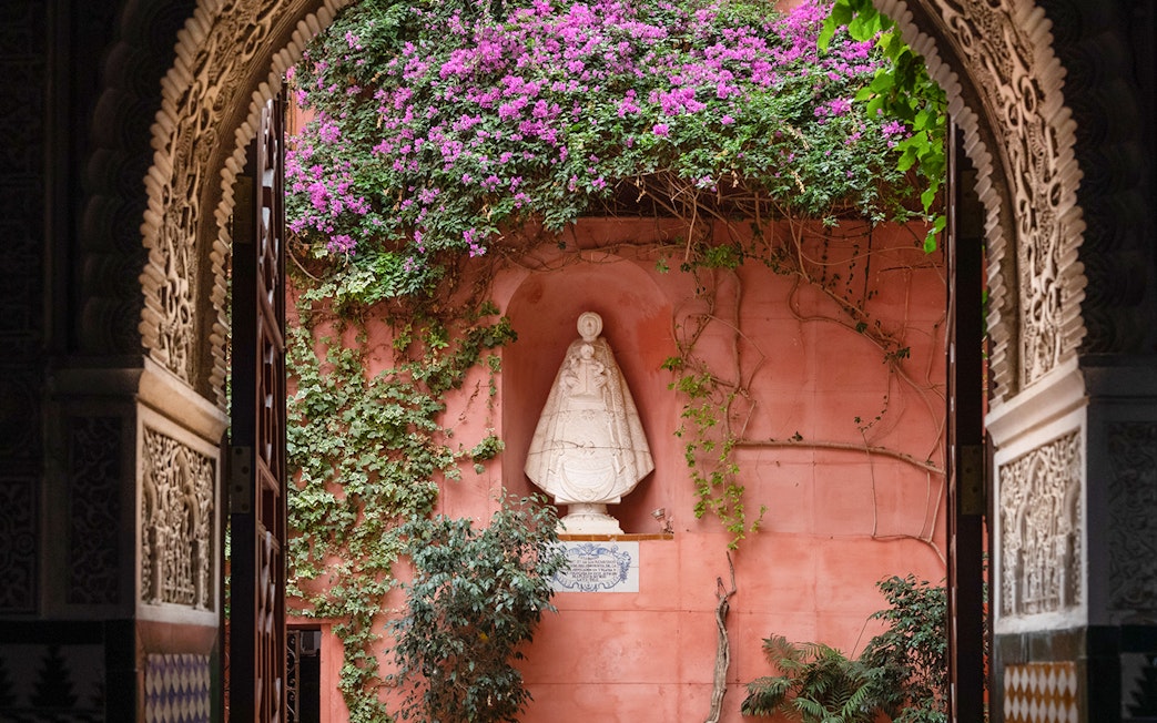 Casa de Salinas archway with ornate carvings, pink wall, and statue surrounded by vines and flowers.