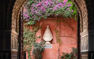 Casa de Salinas archway with ornate carvings, pink wall, and statue surrounded by vines and flowers.