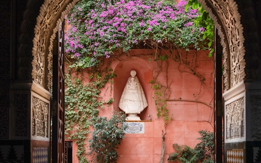 Casa de Salinas archway with ornate carvings, pink wall, and statue surrounded by vines and flowers.