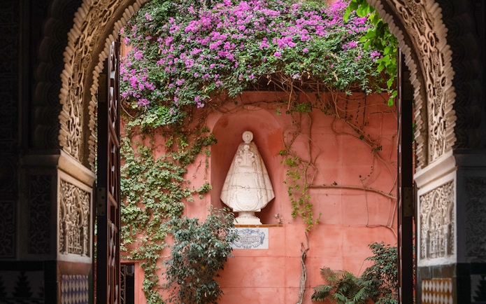 Casa de Salinas archway with ornate carvings, pink wall, and statue surrounded by vines and flowers.