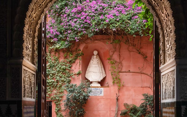 Casa de Salinas archway with ornate carvings, pink wall, and statue surrounded by vines and flowers.