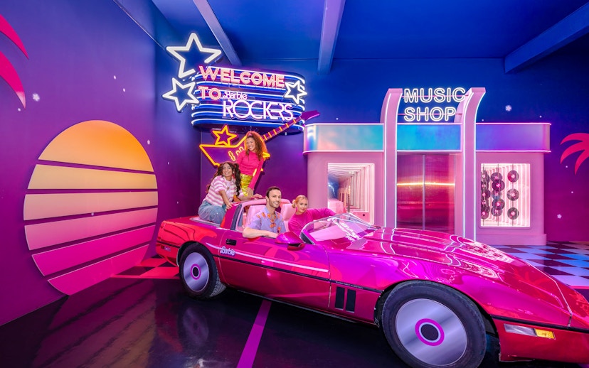 Guests enjoying Barbie, The Dream Experience in a pink convertible at a neon-lit music shop.