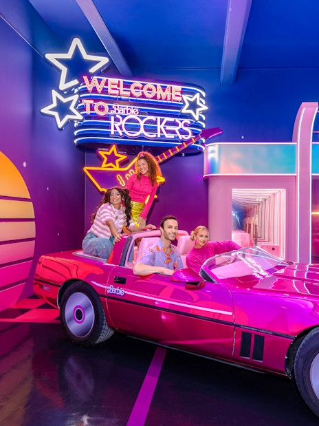 Guests enjoying Barbie, The Dream Experience in a pink convertible at a neon-lit music shop.