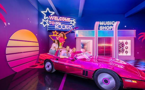 Guests enjoying Barbie, The Dream Experience in a pink convertible at a neon-lit music shop.