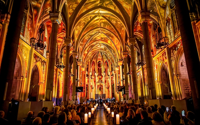 Audience watching LUMINISCENCE Manchester 360° Immersive Show in a cathedral with illuminated arches.