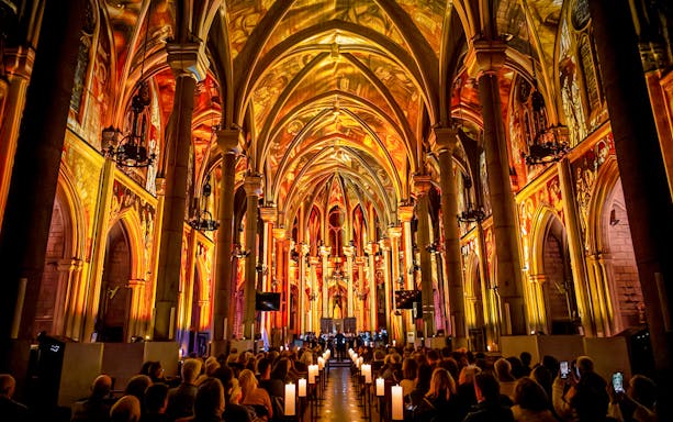 Audience watching LUMINISCENCE Manchester 360° Immersive Show in a cathedral with illuminated arches.