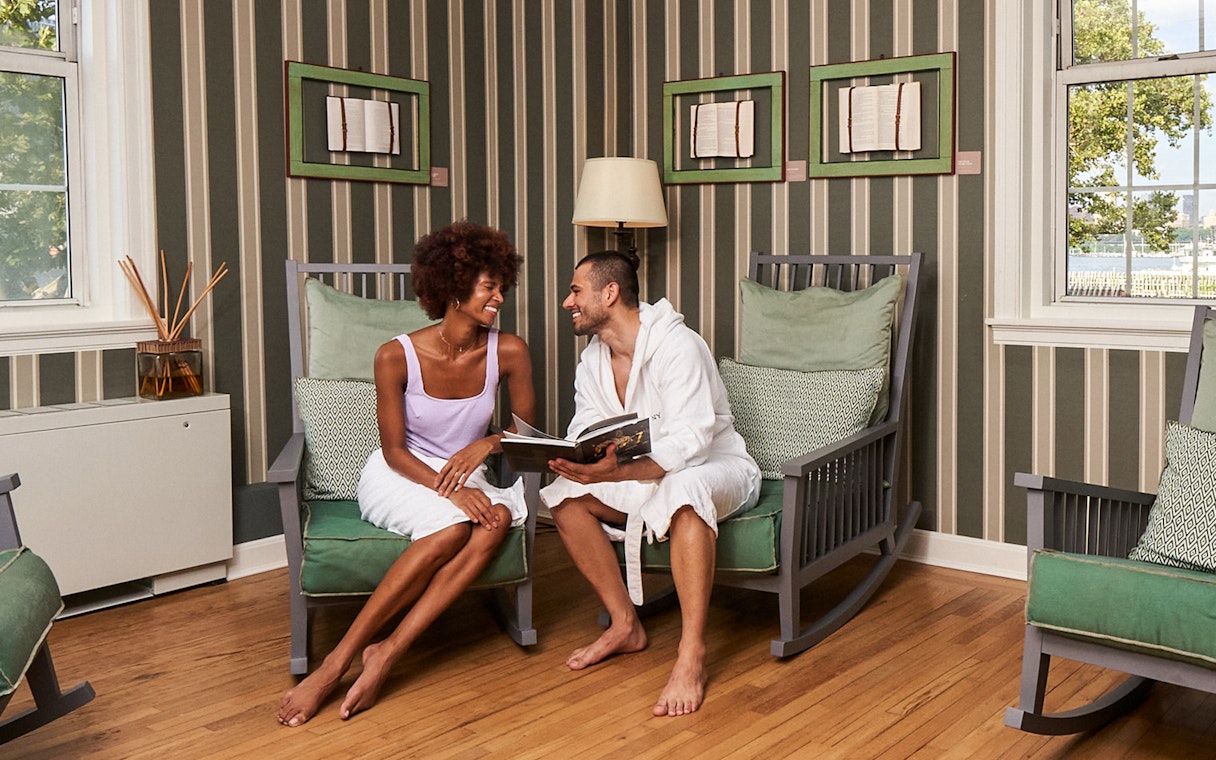 Couple relaxing in a lounge area at QC New York spa, enjoying a book together.