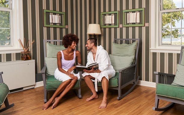 Couple relaxing in a lounge area at QC New York spa, enjoying a book together.