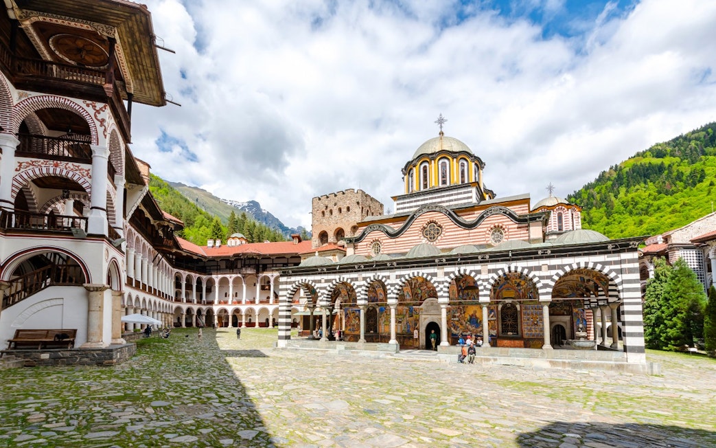 Rila Monastery courtyard with arched frescoes and mountainous backdrop.