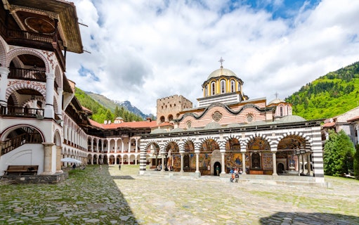 Rila Monastery courtyard with arched frescoes and mountainous backdrop.