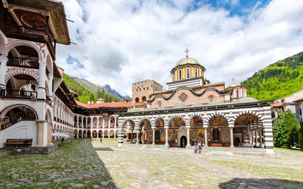 Rila Monastery courtyard with arched frescoes and mountainous backdrop.
