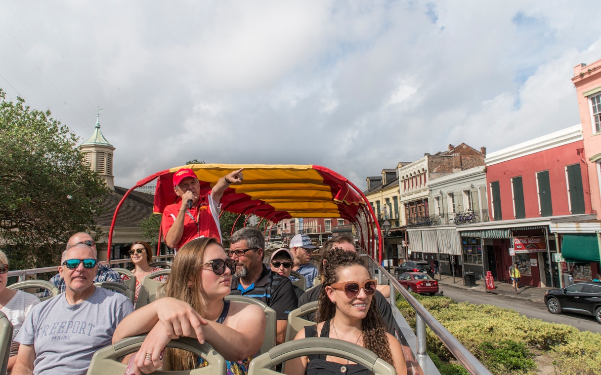 Tourists on a New Orleans hop-on hop-off bus tour with a guide pointing out landmarks.