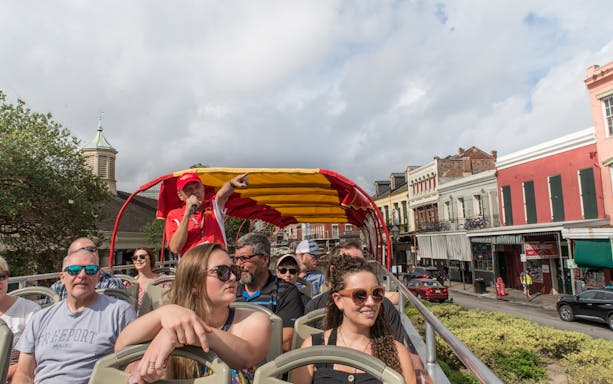 Tourists on a New Orleans hop-on hop-off bus tour with a guide pointing out landmarks.