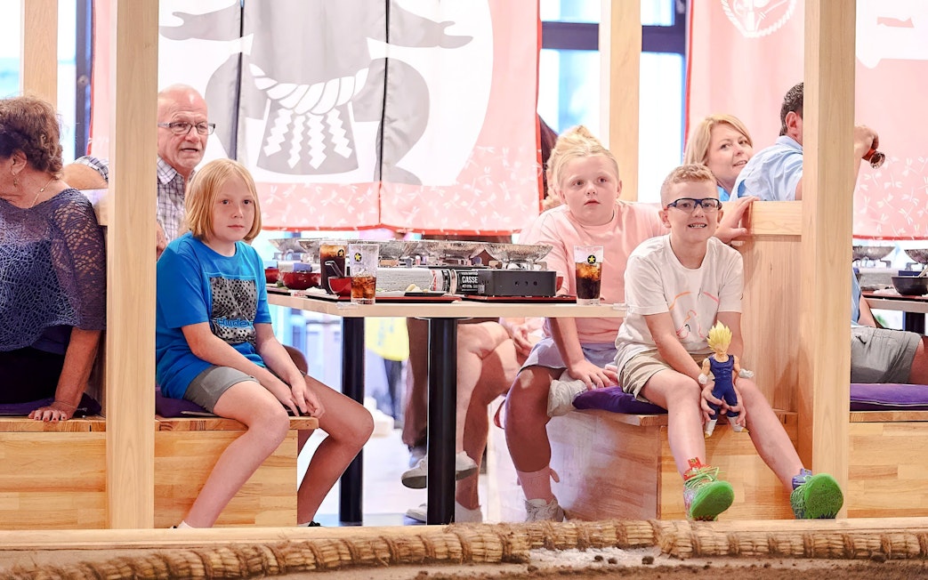 Kids watching a sumo wrestling show at Ryogoku with dining tables in the background.
