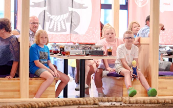Kids watching a sumo wrestling show at Ryogoku with dining tables in the background.