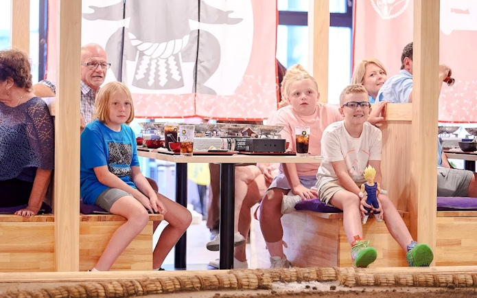 Kids watching a sumo wrestling show at Ryogoku with dining tables in the background.
