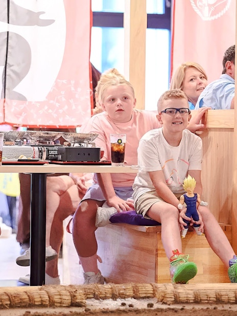 Kids watching a sumo wrestling show at Ryogoku with dining tables in the background.