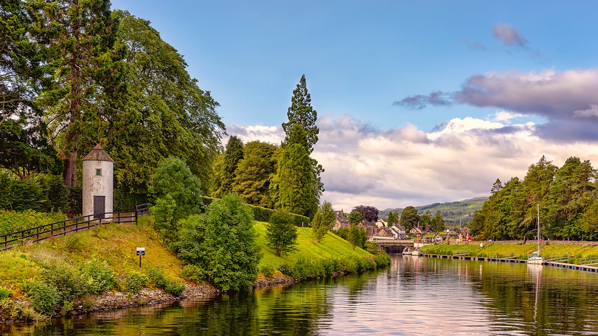 Caledonian Canal with lush greenery and a small tower near the water.
