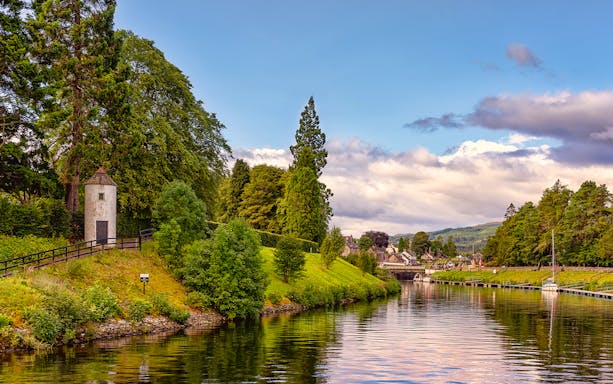 Caledonian Canal with lush greenery and a small tower near the water.
