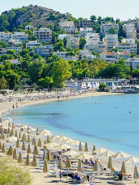 Vouliagmeni Beach in Athens with sun loungers, umbrellas, and a lifeguard tower.