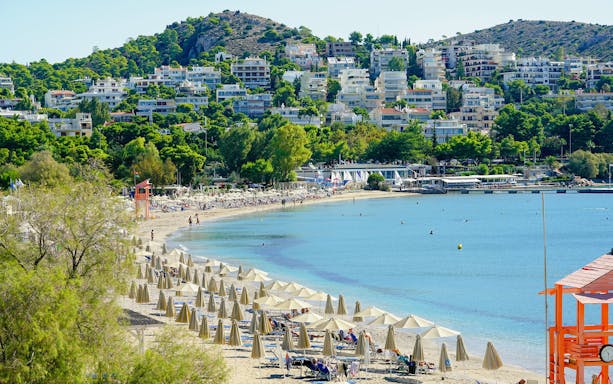 Vouliagmeni Beach in Athens with sun loungers, umbrellas, and a lifeguard tower.