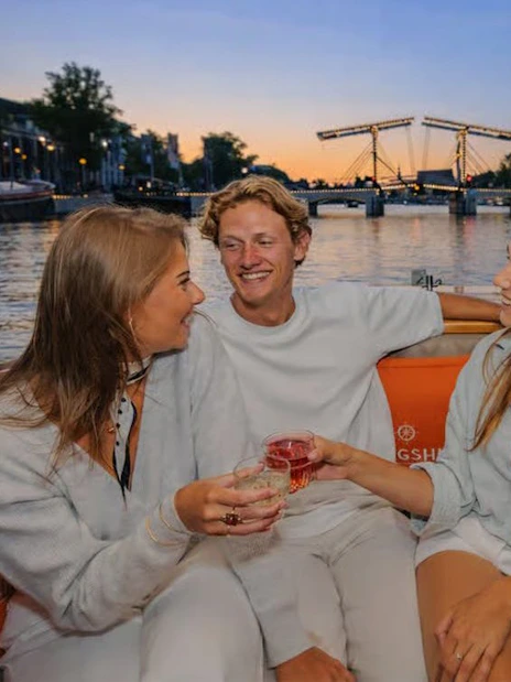 Group enjoying a canal cruise in Amsterdam at sunset with the Magere Brug in the background.