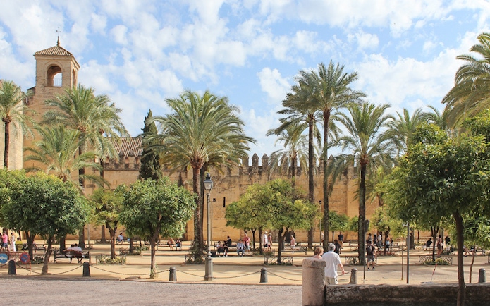Córdoba Cathedral-Mosque courtyard with palm trees and visitors exploring.