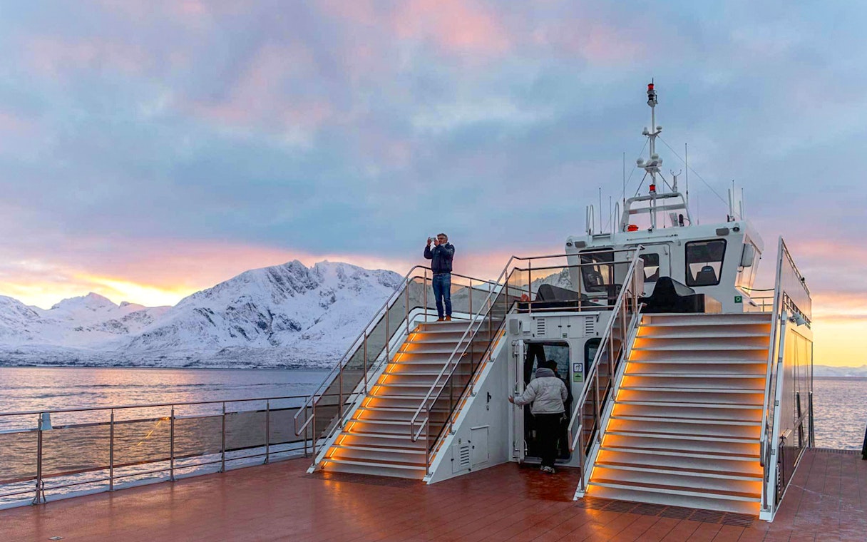 Tourists on a hybrid-electric cruise in Tromso, Norway, with snowy mountains in the background.