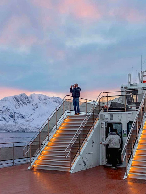 Tourists on a hybrid-electric cruise in Tromso, Norway, with snowy mountains in the background.