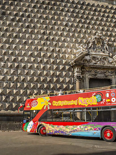Naples hop-on hop-off bus in front of historic building facade.