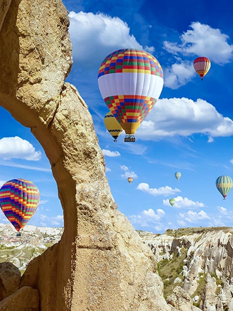 Hot air balloons over Gerome Valley, Cappadocia, with rock formations in the foreground.