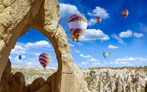 Hot air balloons over Gerome Valley, Cappadocia, with rock formations in the foreground.