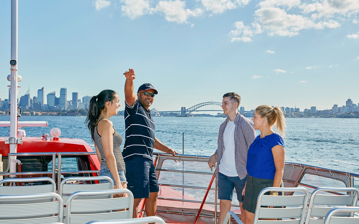 Couple with Captain Cook Sydney Harbour Cruise staff on deck with Sydney skyline.
