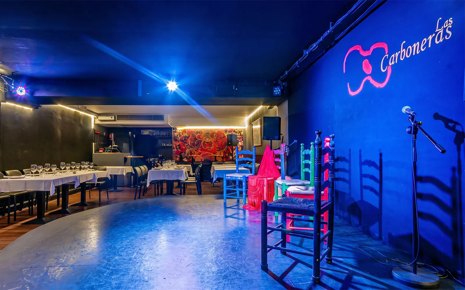 Tablao LAS CARBONERAS stage set for Flamenco show with colorful chairs and microphone.