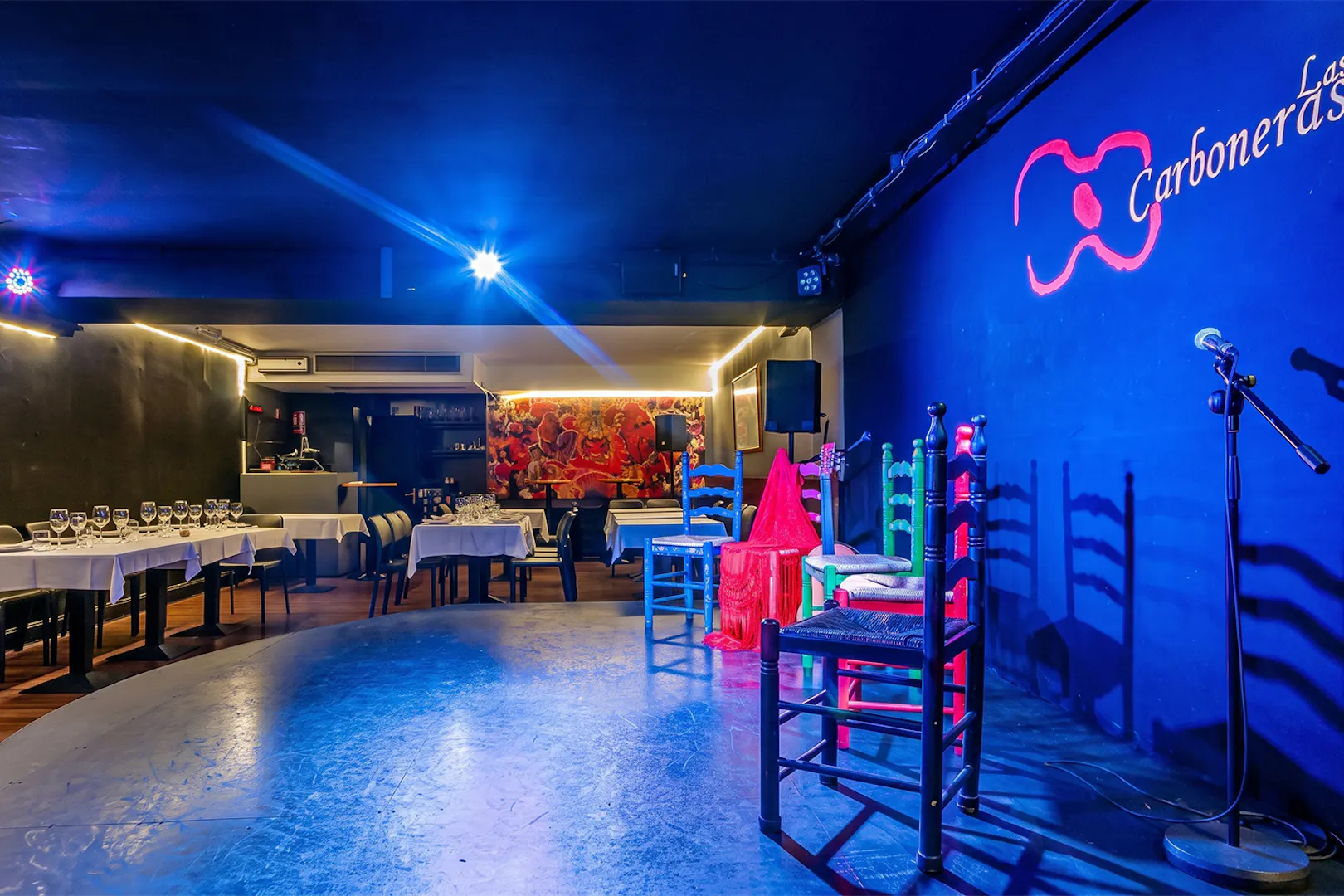 Tablao LAS CARBONERAS stage set for Flamenco show with colorful chairs and microphone.