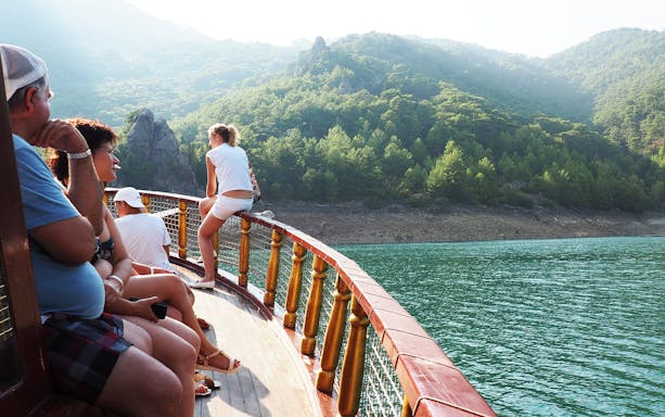 Guided boat tour on Green Canyon, Antalya, with passengers enjoying scenic views of lush hills and water.