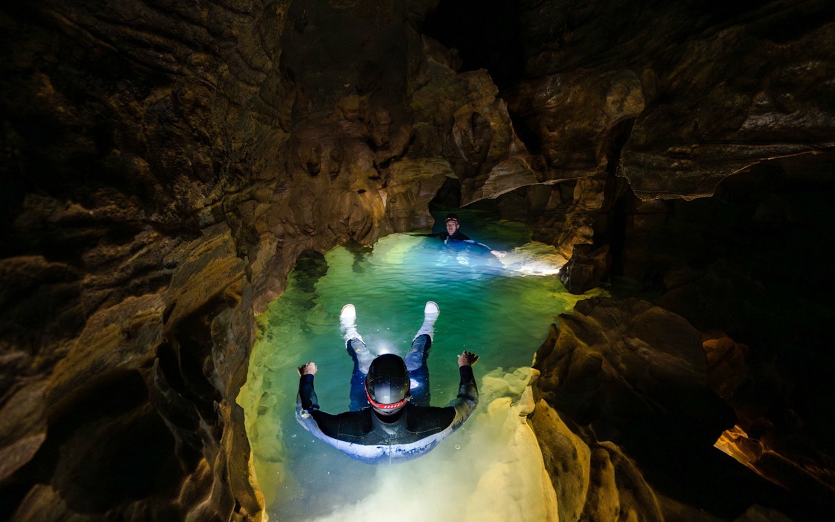 Visitors floating in Okohua Glowworm Cave, illuminated by cave lights, during the Waitomo Experience tour.