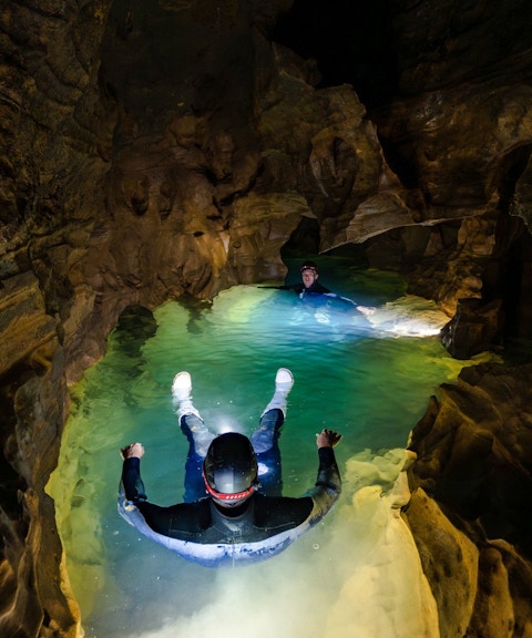 Visitors floating in Okohua Glowworm Cave, illuminated by cave lights, during the Waitomo Experience tour.