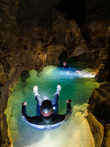 Visitors floating in Okohua Glowworm Cave, illuminated by cave lights, during the Waitomo Experience tour.