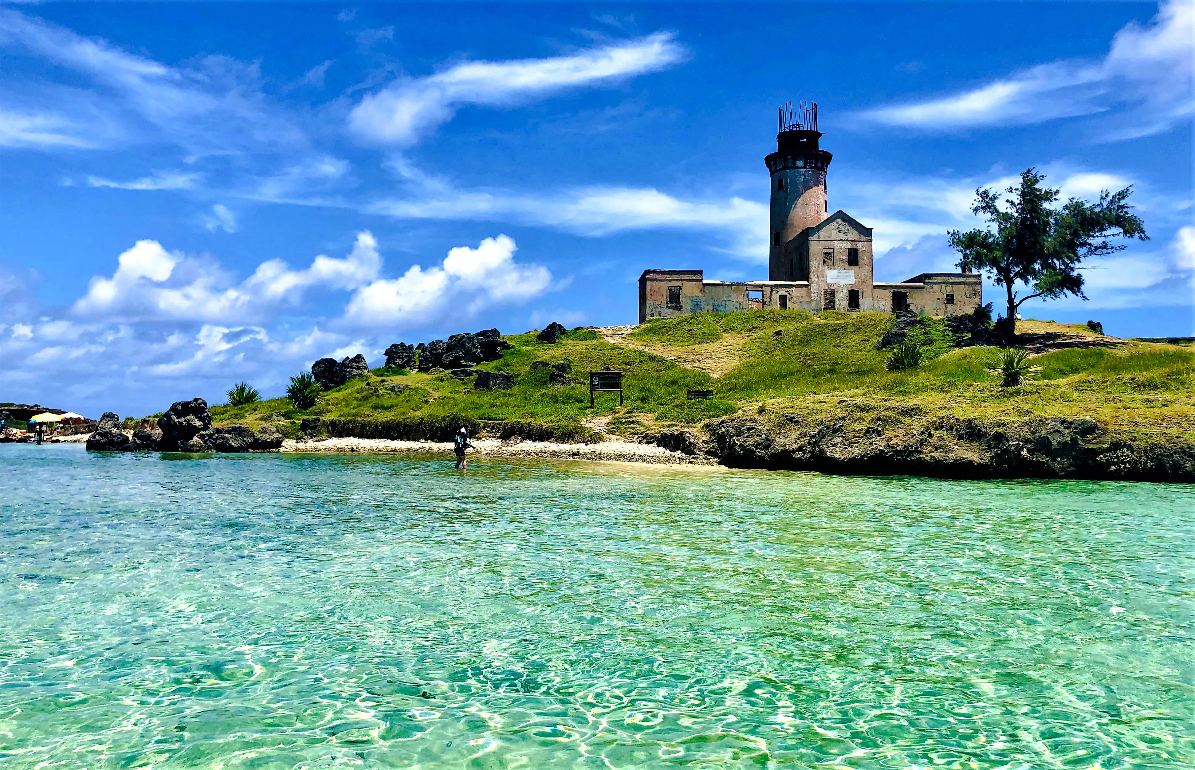 Mahebourg lighthouse on a grassy hill by clear turquoise waters, Mauritius.