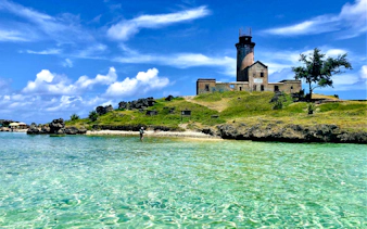 Mahebourg lighthouse on a grassy hill by clear turquoise waters, Mauritius.