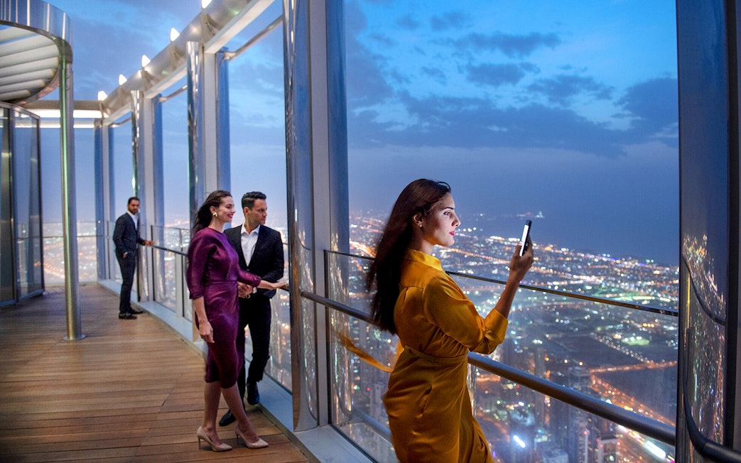 Tourists enjoying the view from the Burj Khalifa lounge in Dubai at night.