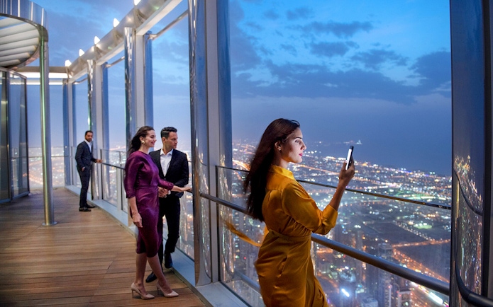 Tourists enjoying the view from the Burj Khalifa lounge in Dubai at night.
