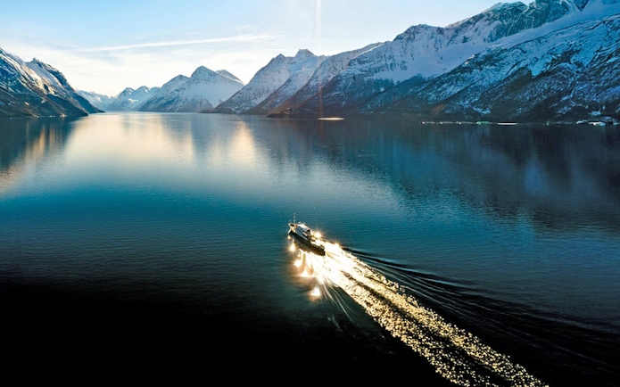 Aerial view of a sightseeing cruise on Hjørundfjord, surrounded by snow-capped mountains in Norway.