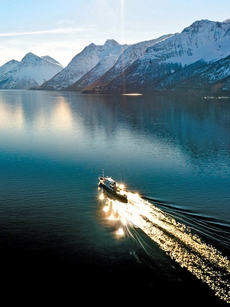 Aerial view of a sightseeing cruise on Hjørundfjord, surrounded by snow-capped mountains in Norway.