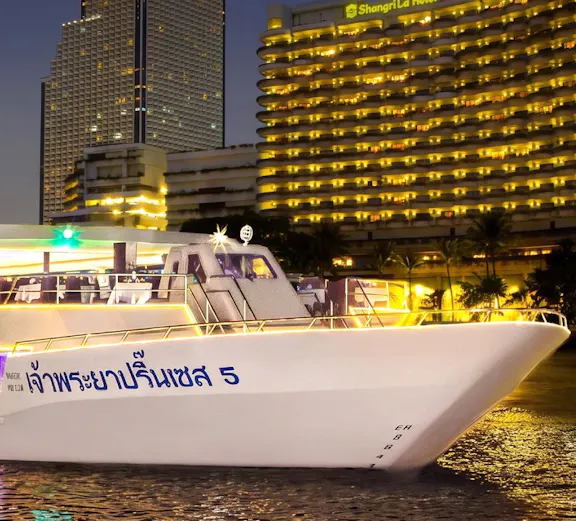 Chao Phraya Princess cruise ship docked near illuminated Bangkok skyline at night.