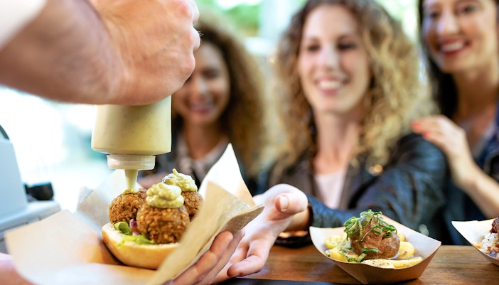 Women receiving food at a market stall, with falafel and sauce being served.